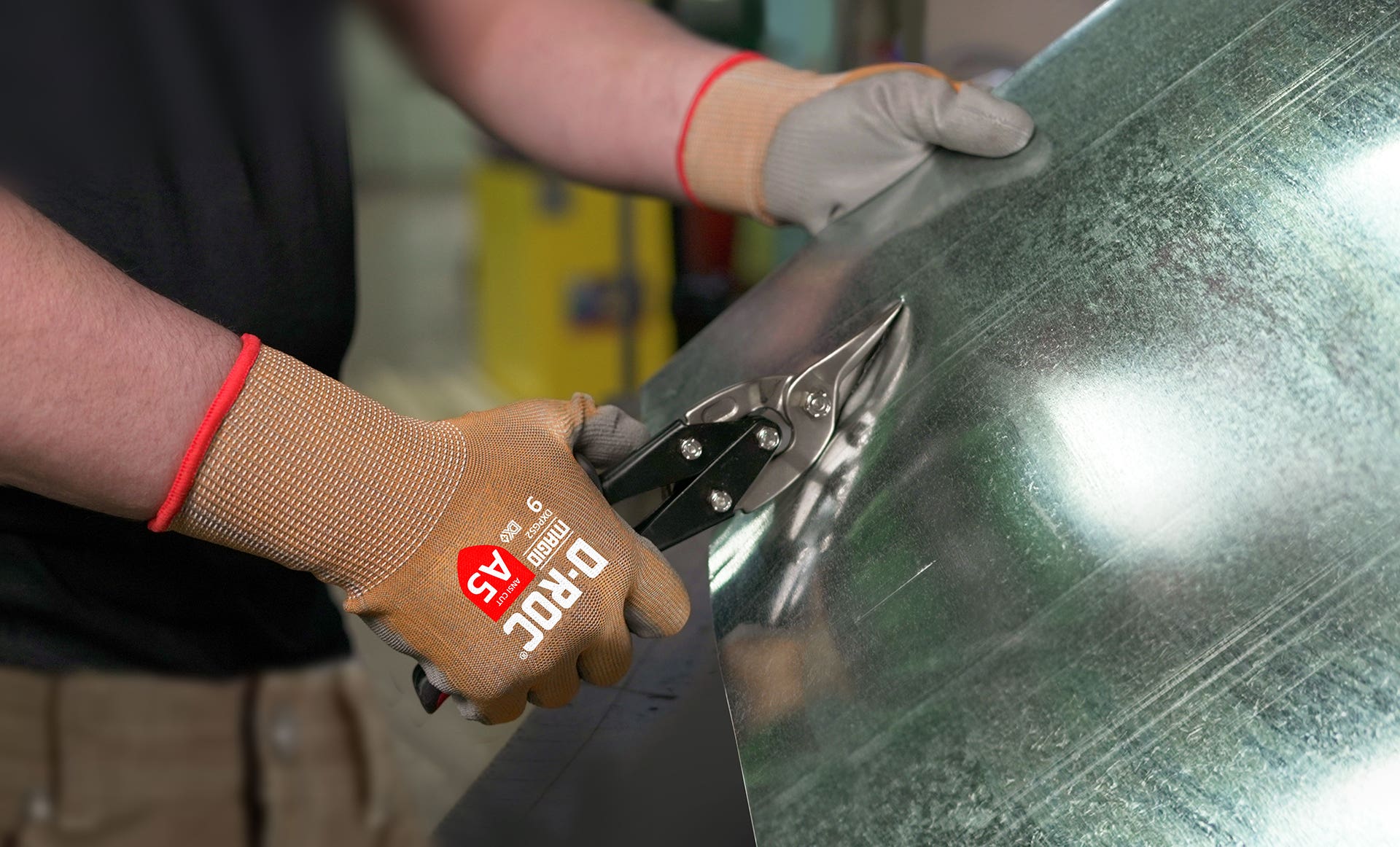 Picture of a worker using tin snips to cut a metal sheet while wearing Magid DXPlus Cut Resistant Gloves