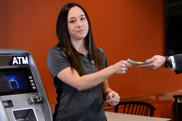 A picture of a woman standing next to an ATM machine, handing money over to a man in a suit sticking his hand into the frame.